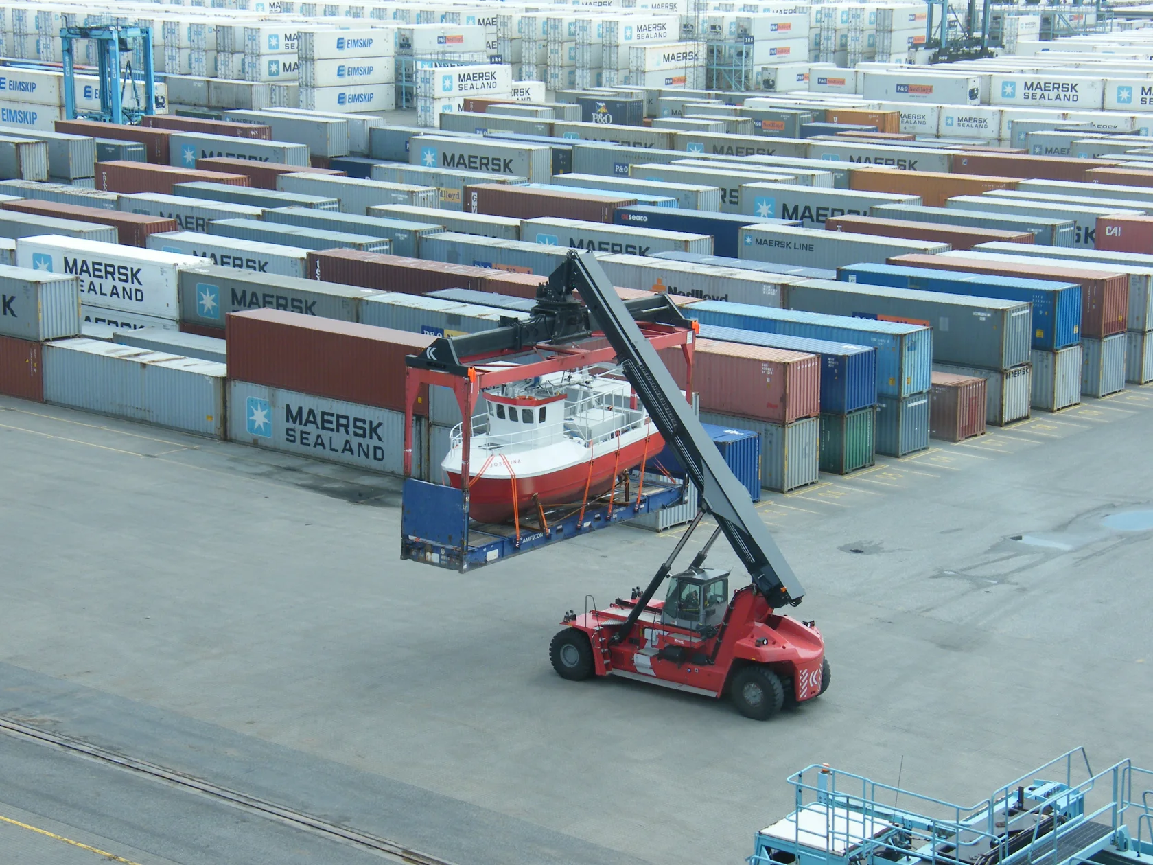 Industry photograph of a small vessel loaded on a flat rack container.